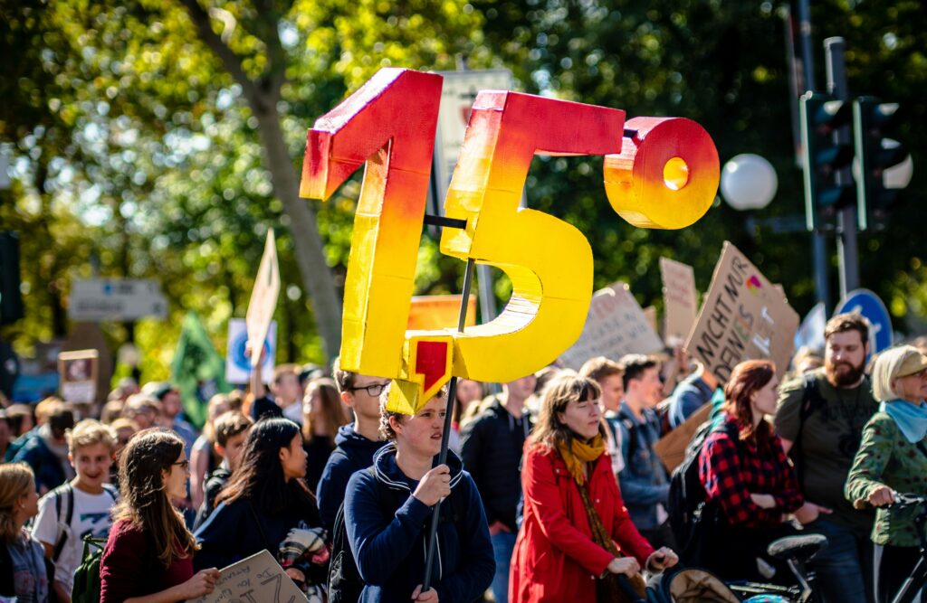 A crowd of people in the street on a sunny day with a sign reading 1.5 degrees. credit: mika-baumeister